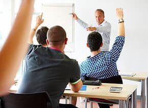 Classroom with teacher asking a question and students raising hands